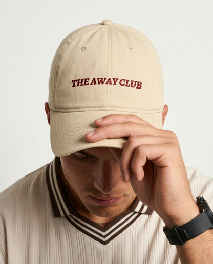 Person wearing a beige cap with 'THE AWAY CLUB' text on a light background
