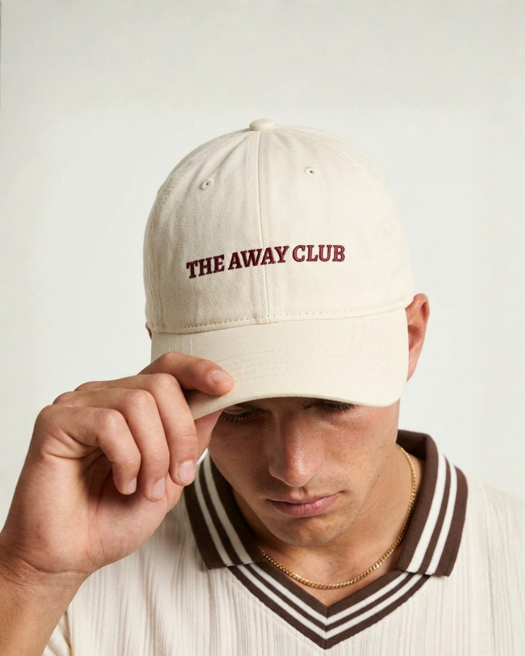 Person wearing a beige cap with 'THE AWAY CLUB' text on a plain background